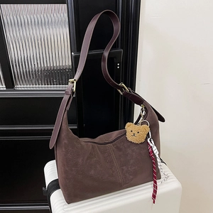 Macro shot of dark brown faux suede dumpling bag with cute plush bear charm on a suitcase