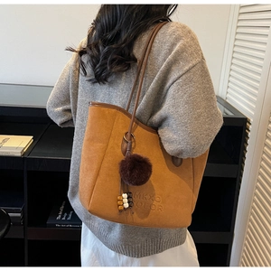 Détail d'un cabas en daim marron avec lettrage embossé et pompon décoratif doux