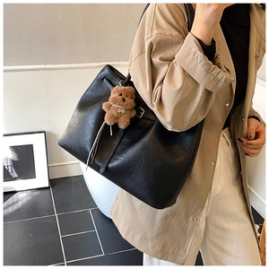 Detail of large black suede tote bag with a brown plush bear charm worn by a model