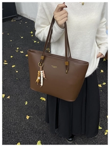 Detail of a brown leather tote bag with elegant beaded tassel and fojy brand lettering