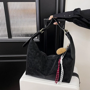 Detail of black large capacity dumpling tote bag with tassel and gold buckle on a suitcase
