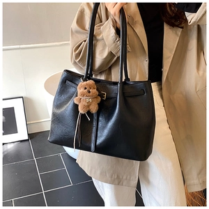 Detail of black faux leather tote bag featuring a teddy bear charm and gold metal buckle