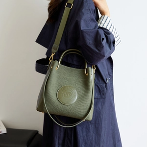 Secchiello verde oliva con trama a coccodrillo e tracolla larga su cappotto blu navy