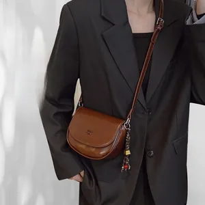 Détail d'un sac besace rétro marron foncé avec pompon et breloque en métal sur le côté