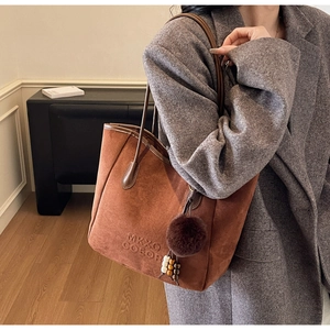 Détail d'un grand sac cabas en daim marron avec pompon en peluche porté avec un tailleur