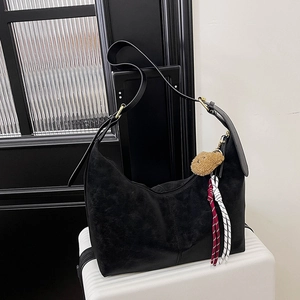 Close-up of black crossbody dumpling bag featuring textured finish and plush bear charm