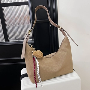 Detail view of khaki half-moon bag with bear charm and striped ribbons on white suitcase