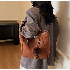 Détail du sac cabas en daim marron foncé avec logo MK gaufré et charm décoratif doux