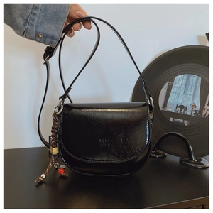 Détail du sac selle noir avec texture plissée brillante et pendentif en corde tressée