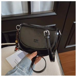 Détail d'un sac besace noir brillant avec lettres embossées et boucles en métal argenté