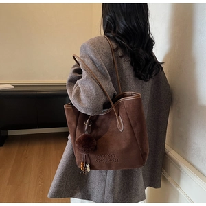 Détail d'un sac cabas en daim marron foncé avec logo embossé et pendentif pompon