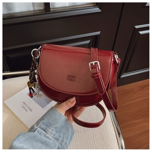 Détail d'un sac besace rouge foncé avec logo embossé et pendentif chaîne argentée décoratif