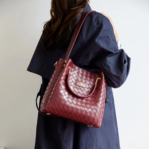 Dettaglio della borsa a secchiello in pelle intrecciata bordeaux con hardware dorato
