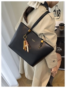 Detail of black leather tote bag with unique multi-strand straps and beaded tassel charm