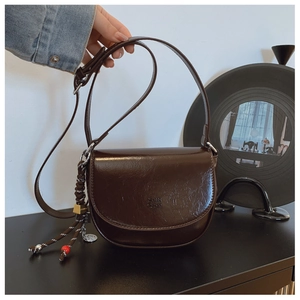 Gros plan sur le sac besace marron foncé avec logo embossé et pendentif en corde tressée