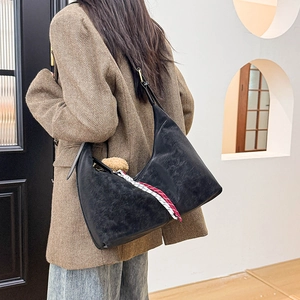 Detail of black vintage leather hobo bag with woven rope and plush pendant decoration