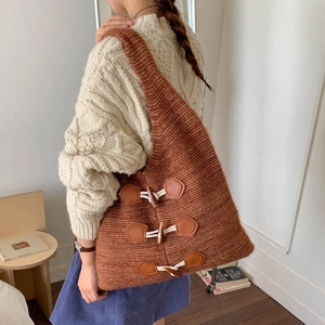 Detail of a brown chunky knit tote bag featuring classic horn buckles and woven texture