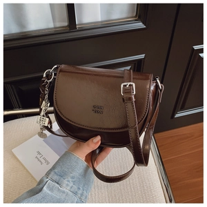 Détail du sac selle marron foncé avec logo embossé et chaîne en argent