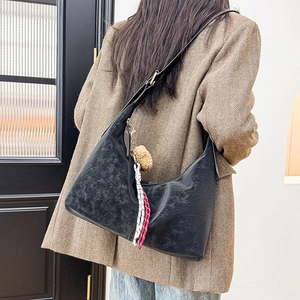 Detail of black wax leather hobo bag with vintage texture and red woven pendant charm