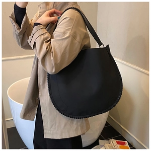 Detail of black half-moon tote bag with woven trim on a model in a stylish beige trench coat