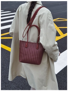 Détail d'un sac seau bordeaux tressé avec poignées en cuir et bandoulière amovible