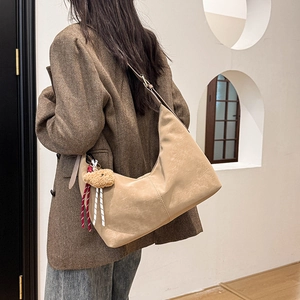 Close-up of beige moon hobo bag with teddy bear charm on shoulder of a female model