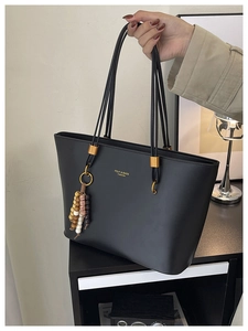 Detail of black matte tote bag with golden metal buckles and colorful beaded tassel charm