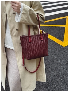 Détail d'un sac cabas bordeaux en cuir tressé avec bandoulière longue dans un décor urbain