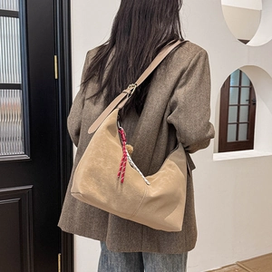 Detail of khaki leather crescent hobo bag with braided tassel worn by a model in a suit