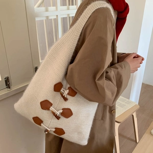 Detail of white knit tote bag featuring brown leather straps and wooden toggle closure