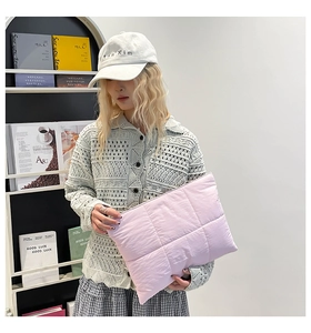 Close-up of a light pink quilted puffer clutch bag being held by a model for a lifestyle view