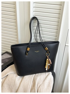 Detail of black leather tote bag featuring gold logo and colorful beaded tassel charm