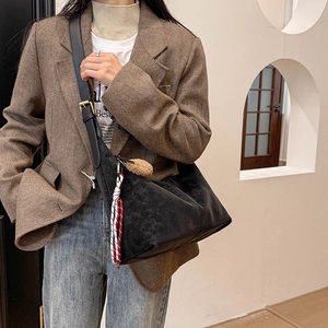Detail of black suede hobo bag with plush ball charm and woven cord on blazer model