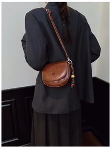 Détail d'un sac besace en cuir marron foncé avec accessoire tissé sur un blazer