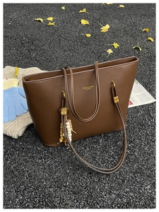 Detail of dark brown tote bag with gold lettering and wooden bead charm on autumn leaves