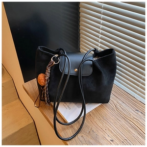 Close-up of black suede tote bag with leather flap, gold snap, and decorative tassel detail