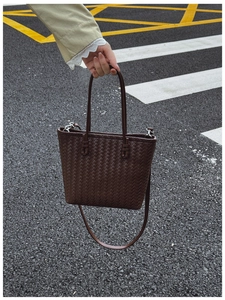 Détail d'un sac seau en cuir tressé marron foncé avec poignées et bandoulière fine