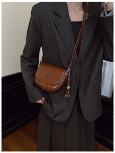 Gros plan sur un sac besace marron en cuir avec pompon porté sur un costume gris