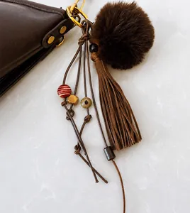 Detail of bohemian bag charm with brown fur pompom and tassels on leather handbag