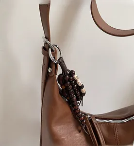 Detail of vintage brown leather bag featuring wooden bead charm and smooth zipper texture