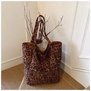Close-up of a large leopard print tote bag with soft suede texture on a woven carpet