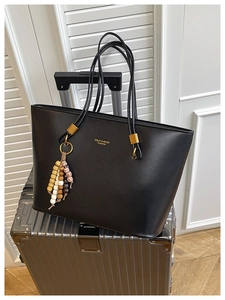 Detail of black leather tote bag with gold lettering and colorful beaded tassel charm