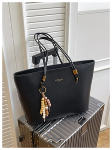 Detail of black faux leather tote bag with gold lettering and beaded tassel on luggage