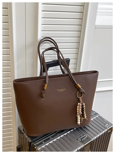 Detail of dark brown tote bag with colorful beaded charm on a silver suitcase