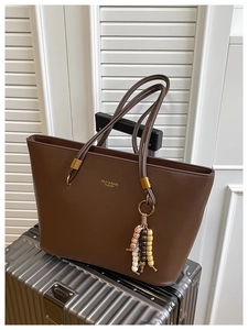 Detail of vintage brown tote bag with beaded charm on silver metal suitcase luggage