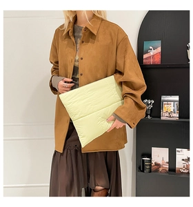 Detailed view of cream-colored quilted puffer clutch bag being held by a model
