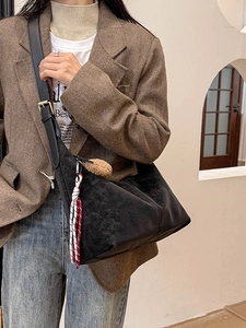 Minimalist black suede hobo bag with wide shoulder strap and decorative brown fur pompom