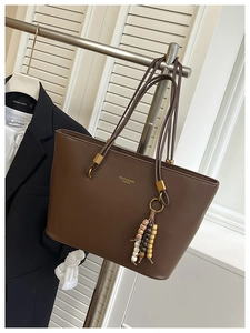 Detail of dark brown leather tote bag with gold lettering and retro beaded pendant