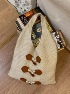 Minimalist beige knitted tote bag with retro toggle closures on light wooden flooring