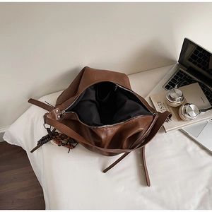 Detailed view of brown leather tote bag with wood bead charm and zipper closure